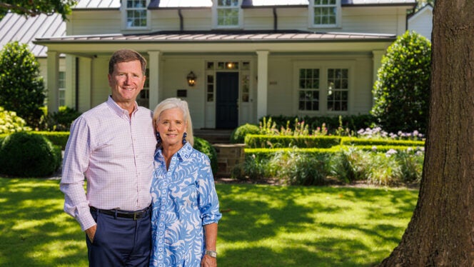 Smiling couple standing in front of a beautiful white house with a well-kept green lawn and garden in Dallas.
