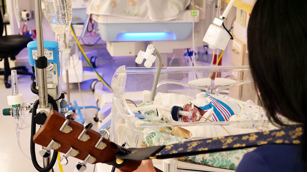 photo of certified music therapist strumming guitar for newborn in nicu at Baylor University Medical Center Dallas