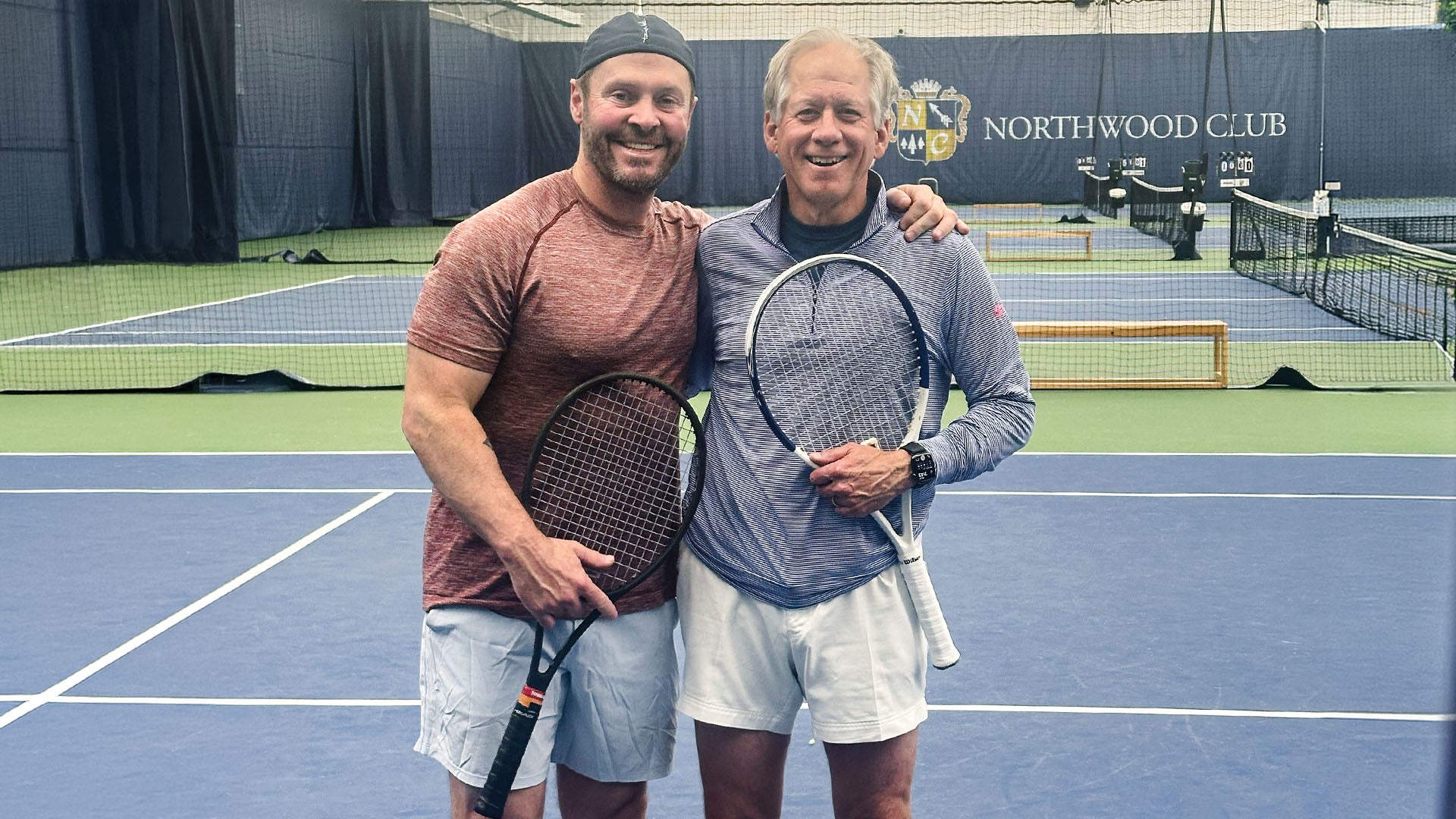 Tim Perry and Dr. Gunn pose with tennis rackets in an indoor tennis court at Northwood Club.