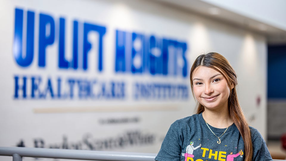 Janelle Lopez, a student at Uplift Heights Healthcare Institute, stands in front of the school's sign as part of Baylor Scott & White Health's partnership to introduce students to healthcare careers.